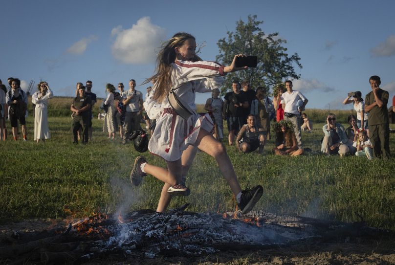 Eine Frau springt bei der traditionellen Mittsommernachtsfeier über das Feuer, Sonntag, 23. Juni 2024. 