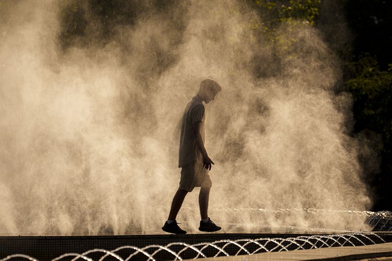 Un jeune homme se rafraîchit dans la bruine d'une fontaine publique, le jeudi 20 juin 2024, alors que les températures dépassent les 38°C