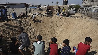 Des enfants palestiniens sont assis au bord d'un cratère après une frappe aérienne israélienne à Khan Younès, dans le sud de la bande de Gaza, le vendredi 21 juin 2024.
