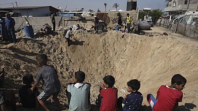 Des enfants palestiniens sont assis au bord d'un cratère après une frappe aérienne israélienne à Khan Younès, dans le sud de la bande de Gaza, le vendredi 21 juin 2024.