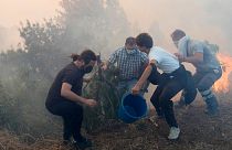 Κάτοικοι χρησιμοποιούν κουβάδες με νερό για να επιβραδύνουν τις φλόγες που πλησιάζουν τα σπίτια τους στο Alcabideche, έξω από τη Λισαβόνα, 25 Ιουλίου 2023.