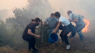 Local residents use buckets with water to try to slow down flames approaching their houses in Alcabideche, outside Lisbon, 25 July 2023.