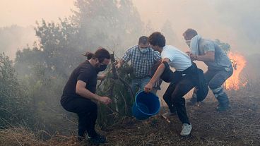 Moradores locais usam baldes com água para tentar abrandar as chamas que se aproximam das suas casas em Alcabideche, nos arredores de Lisboa, a 25 de julho de 2023.