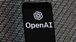 OpenAI logosu, 9 Mart 2023 Perşembe günü Boston'da, rastgele ikili veriler içeren bir bilgisayar ekranının önündeki bir cep telefonunda görünüyor. 