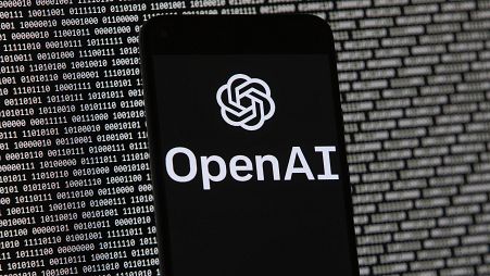El logotipo de OpenAI aparece en un teléfono móvil frente a una pantalla de ordenador con datos binarios aleatorios, el jueves 9 de marzo de 2023, en Boston. 
