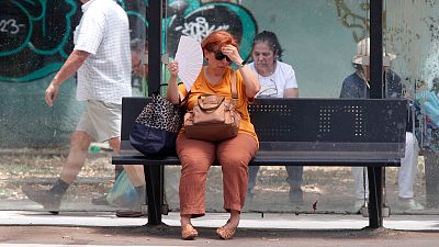 A woman tries to cool herself while waiting for a bus on a hot day in Skopje, North Macedonia, on 20 June 2024. 