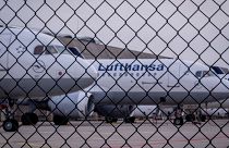 Lufthansa aircrafts are parked behind a fence at the airport in Frankfurt, Germany.