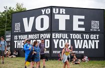 Festivalbesucher laufen während des Glastonbury-Festivals an einem Schild mit der Aufschrift "Your vote is your most powerful tool to get the world you want" vorbei. 