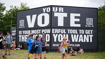 Festival goers walk past a sign that reads "Your vote is your most powerful tool to get the world you want" during the Glastonbury 