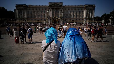 People sit covering their heads from the sun outside Buckingham Palace in the 2022 heatwave. 