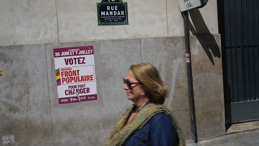 Женщина проходит мимо плаката с надписью "Голосуйте за новый Народный фронт" в преддверии предстоящих парламентских выборов в Париже.
