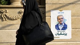 A woman walks past a poster of reformist candidate Masoud Pezeshkian in Tehran, June 29, 2024