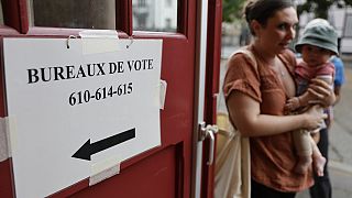 Fransa'nın doğusundaki Strazburg kentinde 30 Haziran 2024 Pazar günü bir kadın çocuğunu oy verme merkezinin dışında tutuyor (AP Photo/Jean-Francois Badias)