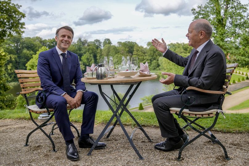 German Chancellor Olaf Scholz, right, and French President Emmanuel Macron sit at a table in the garden of the German government guest house in Meseberg, north of Berlin, Germ