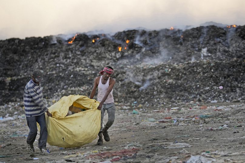 Usmaan Shekh, right, carries, with help, a bag of recyclable material collected from a garbage dump site during a heat wave on the outskirts of Jammu, India