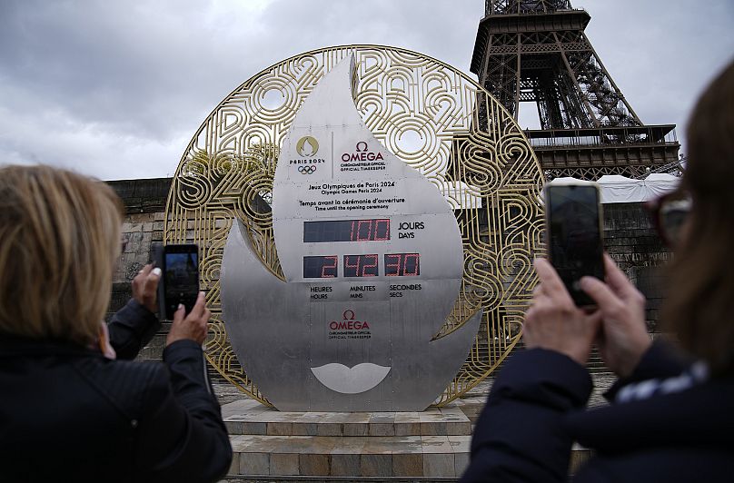 Tourists photograph the clock showing the countdown to the Paris Olympics