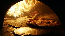 A pizza with a mozzarella cheese topping is cooked in a traditional wood fire oven in downtown Naples.