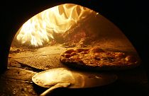Μια πίτσα με επικάλυψη από μοτσαρέλα ψήνεται σε παραδοσιακό φούρνο με ξύλα στο κέντρο της Νάπολης.