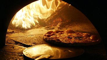 A pizza with a mozzarella cheese topping is cooked in a traditional wood fire oven in downtown Naples.