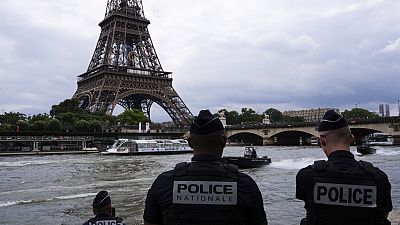 Police officers watch river police boats patroling past the Eiffel Tower, Tuesday, July 2, 2024 on the Seine river in Paris.