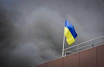 A bandeira ucraniana tremula enquanto se levanta fumo após o ataque de mísseis da Rússia em Dnipro, Ucrânia, quarta-feira, 3 de julho de 2024. (Administração Regional de Dnipro via AP)