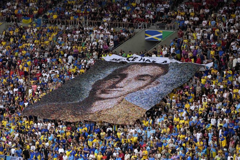 Ukraine fans display a banner reading 'Peace has a price' and a portrait of Nazariy Hryntsevich a fallen soldier a football fan, during match between Ukraine and Belgium