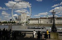 People have their pictures taken on the north bank of river Thames, against the backdrop of the London Eye, in London, Monday, June 17, 2024. (AP Photo/Alberto Pezzali)
