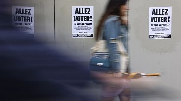 A woman walks past poster reading "Vote" ahead of the second round of the second round of elections on Sunday, 7 July 2024