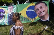 A woman walks past a banner featuring the Brazilian national flag and an image of former President Jair Bolsonaro.