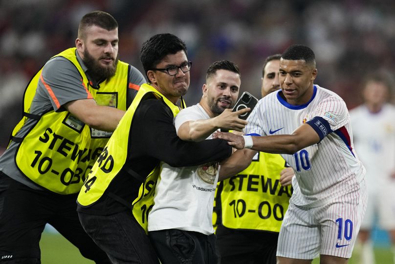 Kylian Mbappé aiuta gli steward a rimuovere uno spettatore che ha fatto irruzione in campo durante la semifinale degli Euro 2024 tra Spagna e Francia a Monaco, 9 luglio 2024