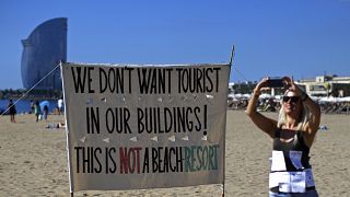 صورة على شاطئ في برشلونة كتب عليها "لا نريد سياحا في مبانيناهذا ليس منتجعا"