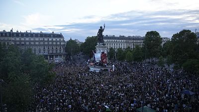 Des personnes se tiennent sur la place de la République en France et réagissent à la projection des résultats du second tour des élections législatives.