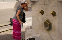Eine Frau kühlt sich ab, während eine Taube Wasser aus einem öffentlichen Brunnen in Belgrad, Serbien, trinkt, 21. Juni 2024. 