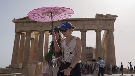 Tourists with an umbrella walk in front of the Parthenon at the ancient Acropolis in central Athens, June 12, 2024. 