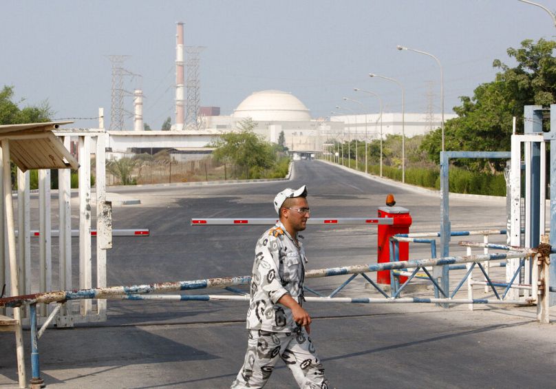 Ein iranischer Sicherheitsbeamter geht an einem Tor des Kernkraftwerks Bushehr vorbei, während im Hintergrund das Reaktorgebäude zu sehen ist.