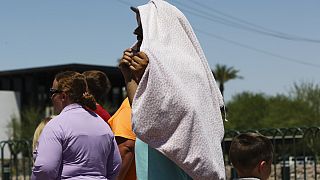 شخص يستخدم بطانية لحجب الشمس أثناء انتظاره لالتقاط صورة عند لافتة "مرحبًا بكم في لاس فيغاس" يوم الاثنين 8 يوليو 2024 