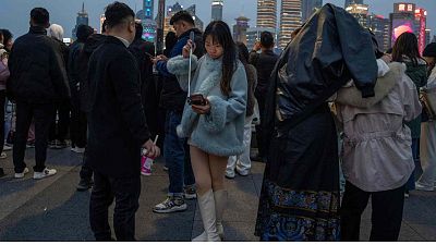 Una mujer mira su teléfono en un palo selfie en el bund, un histórico barrio ribereño de Shanghái conocido por su arquitectura occidental, el 18 de marzo de 2024.