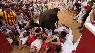 Uma vaca salta sobre um grupo de foliões deitados no chão da praça de touros durante o quarto dia da corrida de touros nas festas de San Fermín em Pamplona.