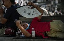 رجل يحاول تبريد جسده بمروحة بينما يتصفح هاتفه الذكي على مقعد في يوم شديد الحرارة في بكين، الأحد، 16 يوليو 2023