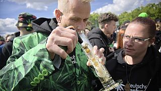 Ένας άνδρας καπνίζει ενώ ο κόσμος πανηγυρίζει στην Πύλη του Βρανδεμβούργου κατά τη διάρκεια μιας συγκέντρωσης και ενός φεστιβάλ για τη νομιμοποίηση της κάνναβης, στο Βερολίνο τον Απρίλιο.