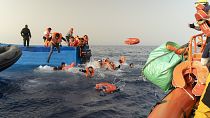 متطوعو منظمة SOS Mediterranee، إلى اليمين، يساعدون في نقل الركاب من قارب مهاجرين خشبي إلى سفينة الإنقاذ الخاصة بهم في البحر الأبيض المتوسط