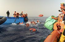 متطوعو منظمة SOS Mediterranee، إلى اليمين، يساعدون في نقل الركاب من قارب مهاجرين خشبي إلى سفينة الإنقاذ الخاصة بهم في البحر الأبيض المتوسط