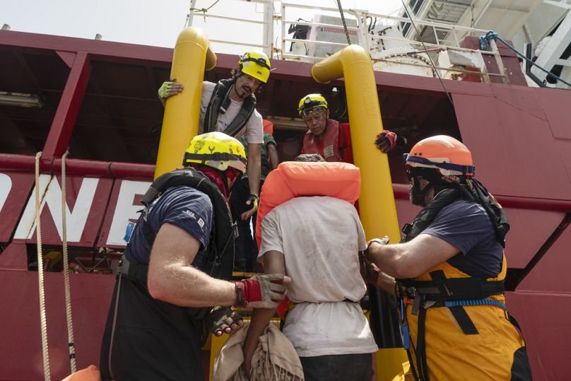 Freiwilligen Helfer von SOS Méditerranée helfen Menschen von einem Holzboot auf ihr eigenes Rettungsschiff im Mittelmeer Juli 2024., 