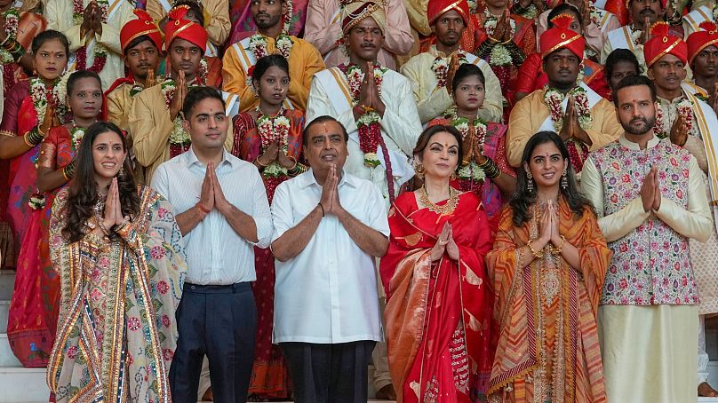 Mukesh Ambani, third left, poses with his family members and underprivileged couples during a mass wedding organized by him as the part of pre-wedding celebrations of his son