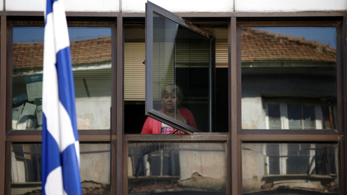 FILE - A municipal worker looks out a window of an occupied municipal building behind a Greek flag in central Athens, on Wednesday, July 10, 2013.