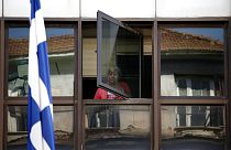 FILE - A municipal worker looks out a window of an occupied municipal building behind a Greek flag in central Athens, on Wednesday, July 10, 2013.
