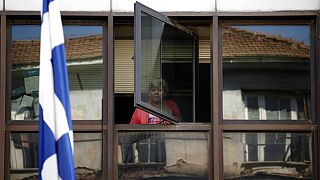 FILE - A municipal worker looks out a window of an occupied municipal building behind a Greek flag in central Athens, on Wednesday, July 10, 2013.