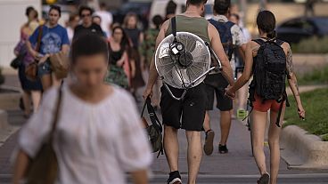  فتاة تمشي ممسكة بيد رجل يحمل مروحة كهربائية على ظهره في أمسية حارة في بوخارست، رومانيا، 25 يوليو 2023. 