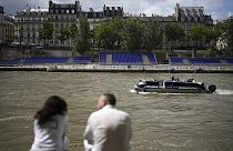 Pessoas sentadas ao longo do rio Sena com bancadas instaladas nas suas margens, 4 de julho 2024