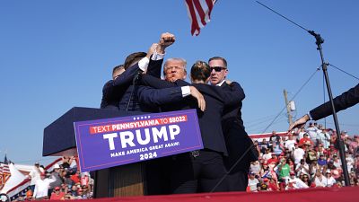 Former President Donald Trump gestures as he is surrounded by Secret Service agents as he leaves the stage in Butler, July 13, 2024